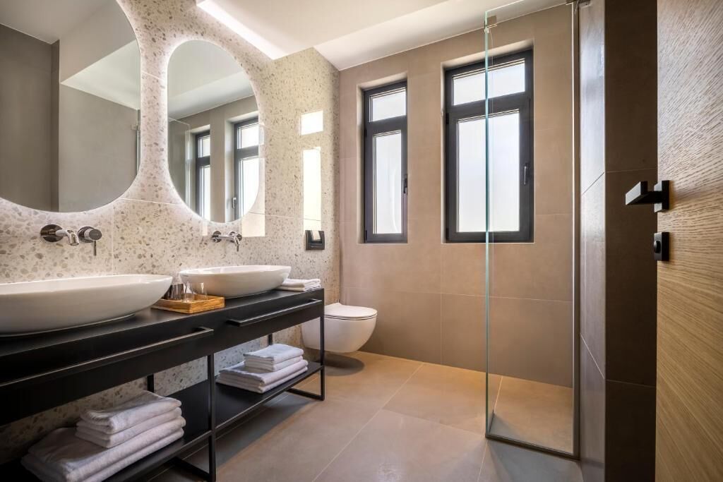 Une salle de bain moderne avec deux grands lavabos, une douche à l’italienne en verre et un grand miroir.