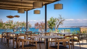 An outdoor dining area with round tables and chairs, hanging pendant lights, and a view of the sea. - DUNATOVI DVORI Heritage Hotel (Preko)