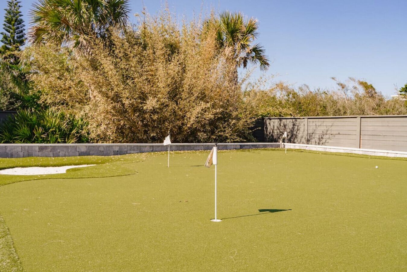 A well-maintained golf course with a putting green, sand bunkers, and a clear sky.