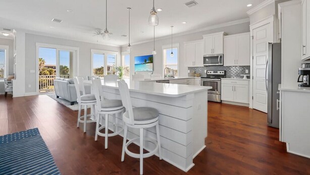 Een moderne keuken met witte kasten, een centraal eiland met barstoelen, roestvrijstalen apparatuur en een groot raam met uitzicht op een balkon.