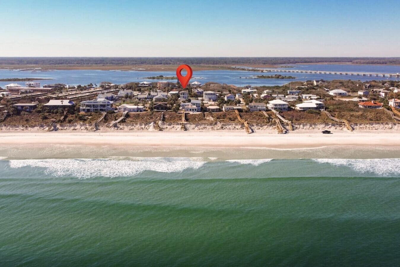 Vue aérienne d’une zone côtière avec une plage, des maisons et un pont au loin.