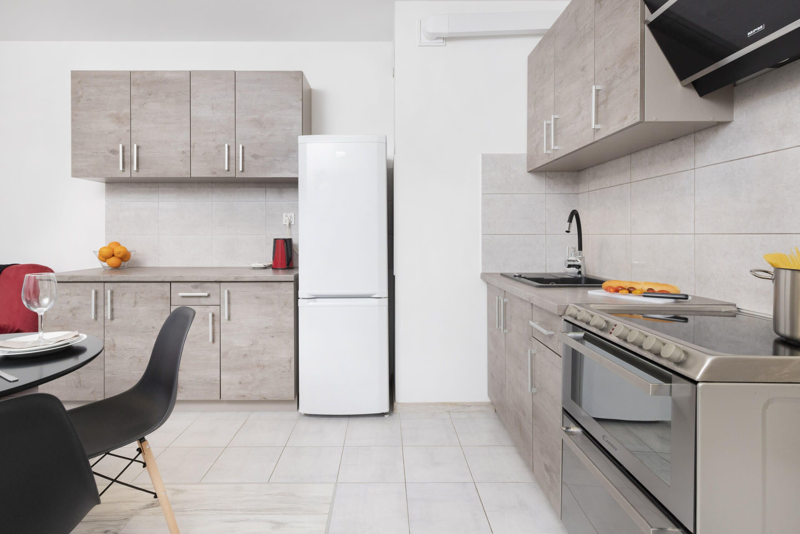 The dining table seamlessly connects with the modern kitchen, equipped with wooden cabinets, a stove, and sleek appliances.

