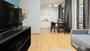 A modern living room with a flat-screen TV, a grey sofa, and a dining area with a table and chairs.