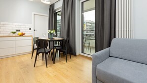 A modern kitchen with a dining area, a grey sofa, and a view of the city through large windows.