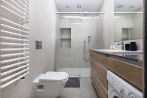Uma casa de banho moderna com cabine de duche em vidro, sanita, máquina de lavar roupa e toucador com espelho.
