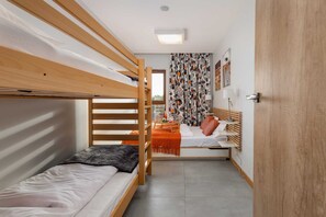 Una habitación con literas, una mesita con lámpara y una ventana con cortinas.
