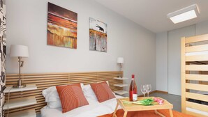 A hotel room with a bed, two paintings, a table with a bottle and glasses, and a wooden bench. - Seaside Apartment with Sea View | Parking and Balcony (Dziwnówek)