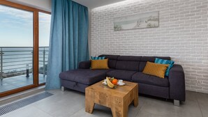 A modern living room with a sofa, a coffee table, and a view of the sea through a large window. - Seaside Apartment with Sea View | Parking and Balcony (Dziwnówek)