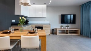 A modern kitchen with white cabinets, a dining table set with plates and glasses, and a flat-screen TV mounted on the wall. - Seaside Apartment with Sea View | Parking and Balcony (Dziwnówek)