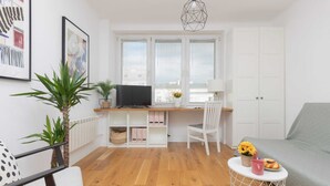 Un salon moderne avec un plancher en bois, un canapé blanc, une table à manger avec une chaise, un téléviseur et une plante.