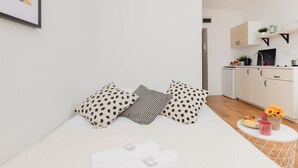 Une chambre à coucher moderne avec un lit, des oreillers, une table de chevet et une petite table ronde sur laquelle se trouve un plateau de petit-déjeuner.