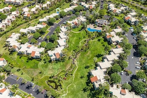 An aerial view of a residential area with houses, a swimming pool, and a landscaped park.