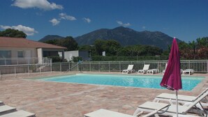 Una piscina con lettini e un ombrellone viola, circondata da un patio in pietra e con una catena montuosa sullo sfondo.