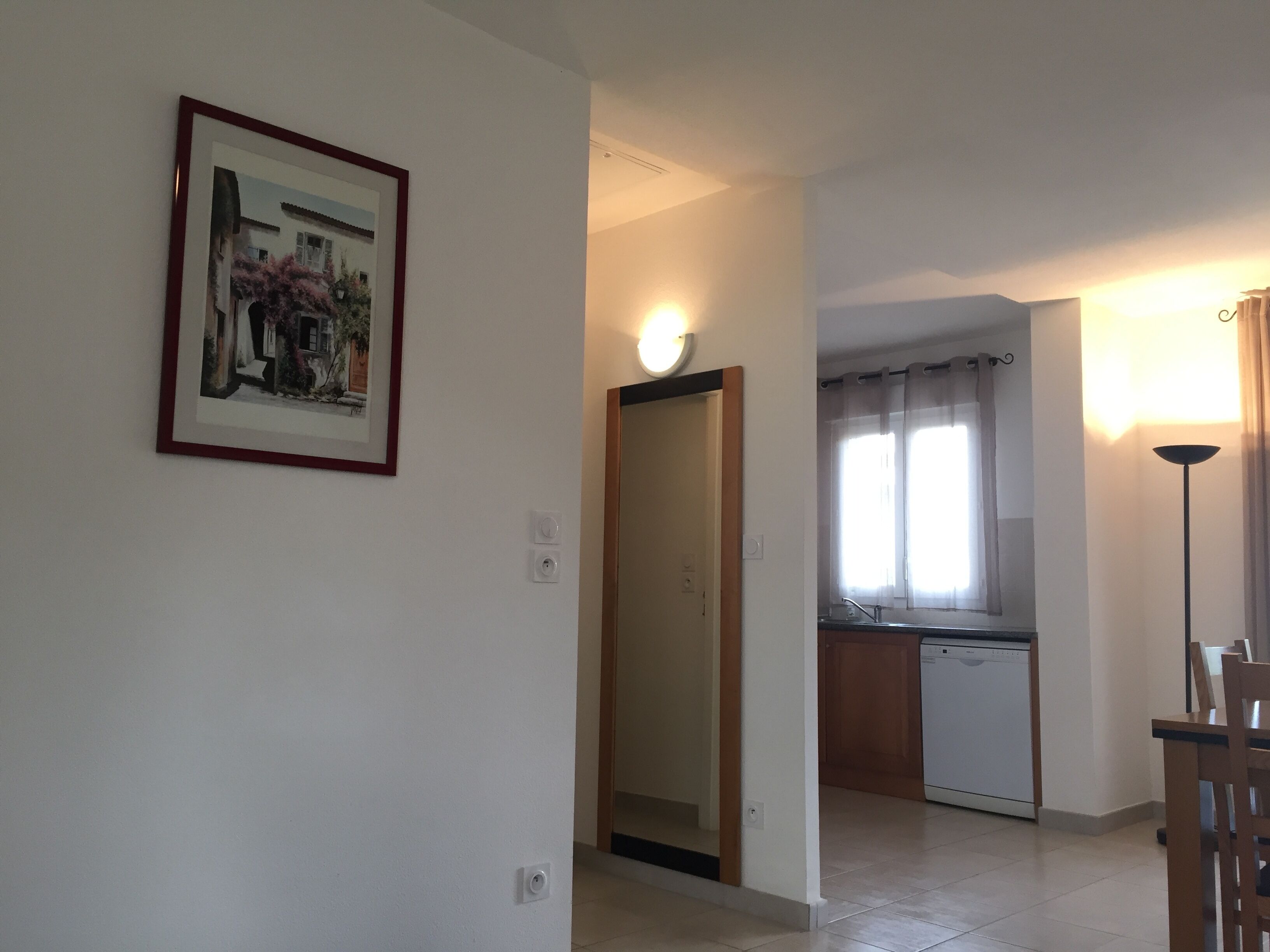 A hallway leading to a kitchen with a dishwasher, a dining area with a table and chairs, and a framed picture on the wall.
