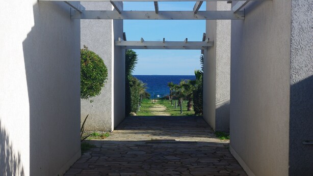 Un vialetto in pietra conduce a una spiaggia attraverso un pergolato bianco.