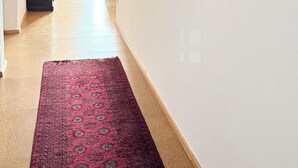 Ein Flur mit Teppich in rotem Muster, weißen Wänden und drei Bildern.
