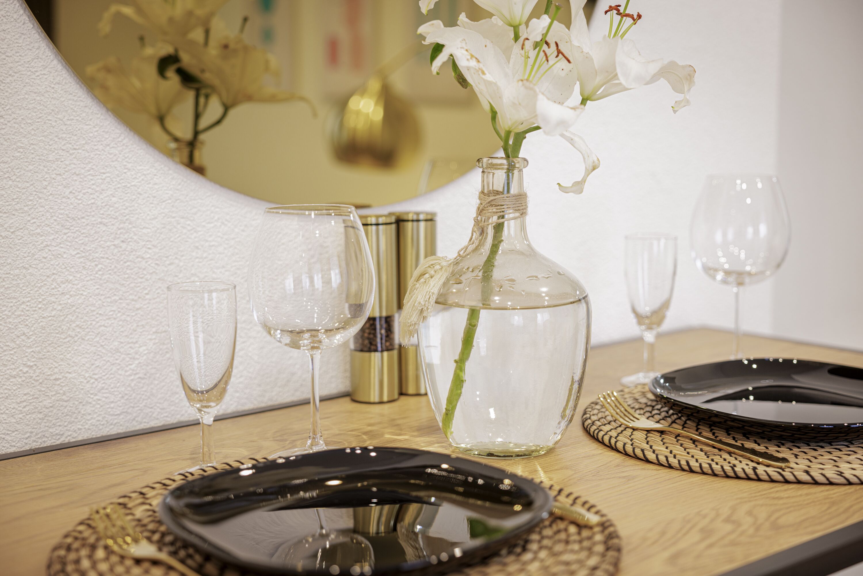 A table set with a black plate, a clear glass, and a vase with white flowers.