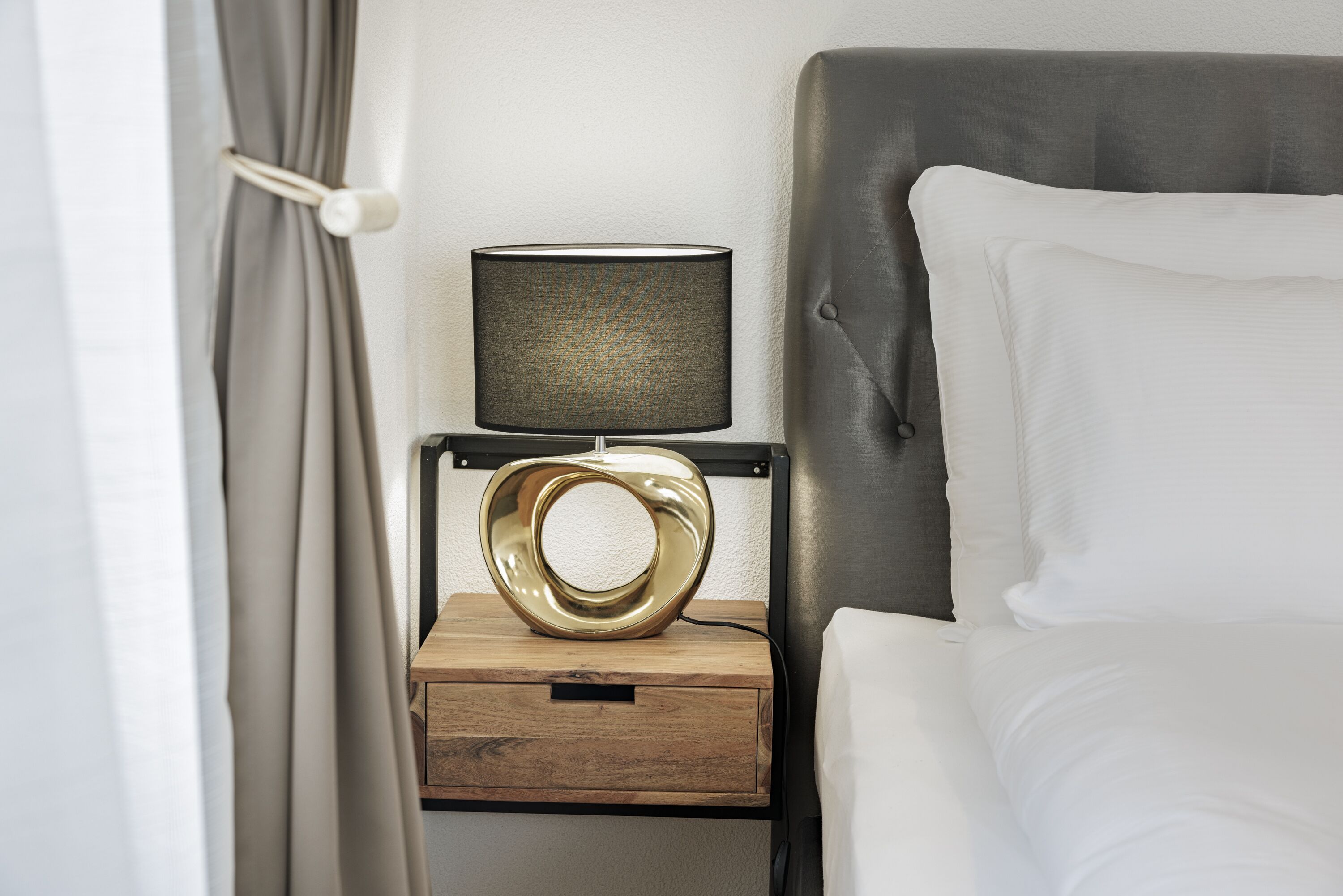 A neatly made bed with white linens, a bedside table with a lamp, and a wooden nightstand.