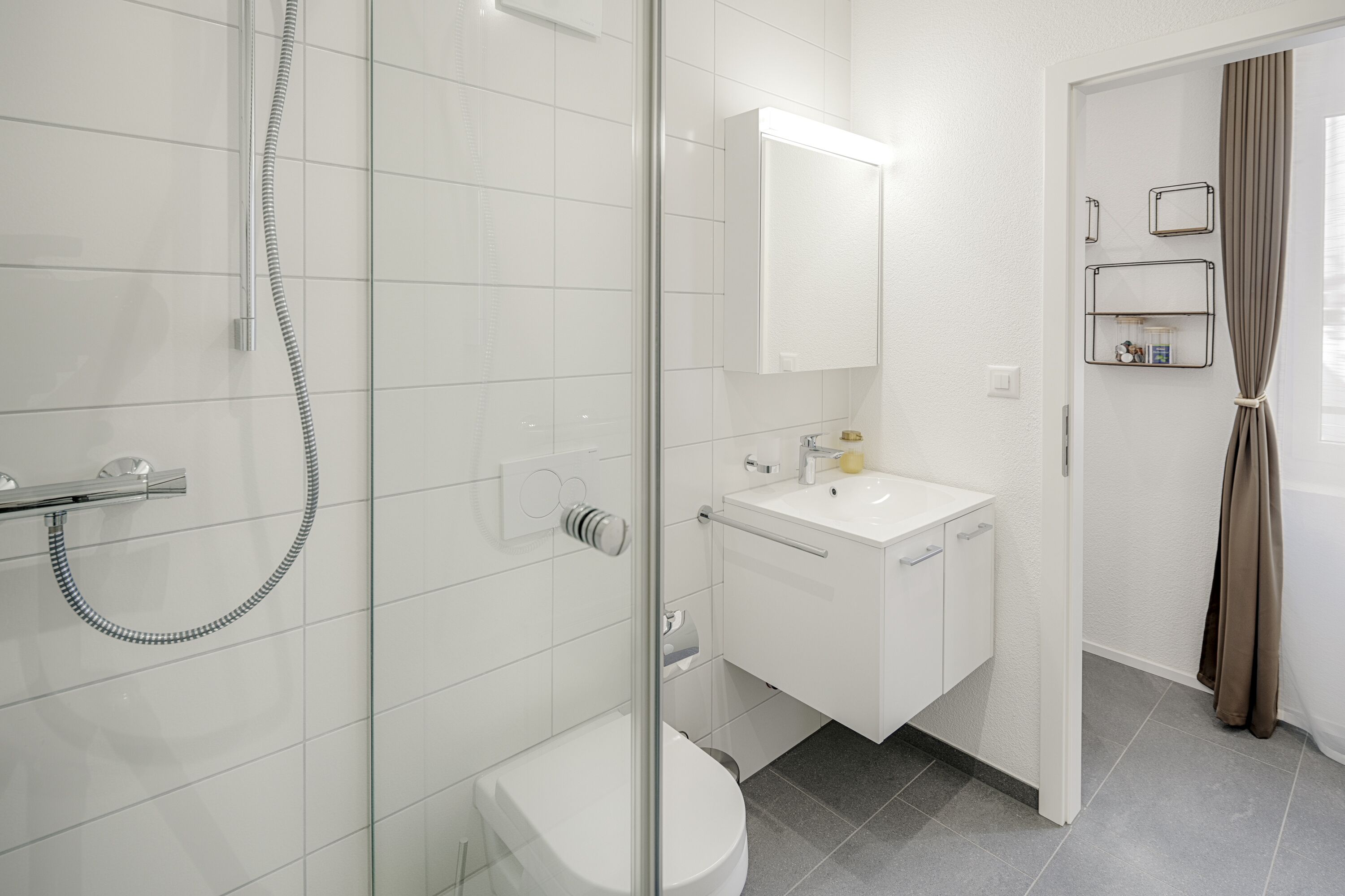 Un bagno moderno con cabina doccia in vetro, lavandino bianco e specchio sopra al lavandino.