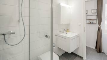 Un bagno moderno con cabina doccia in vetro, lavandino bianco e specchio sopra al lavandino.