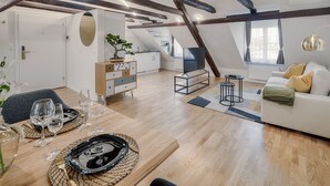 Un comedor con una mesa de madera dispuesta para una comida, un sofá con cojines y una cocina al fondo.