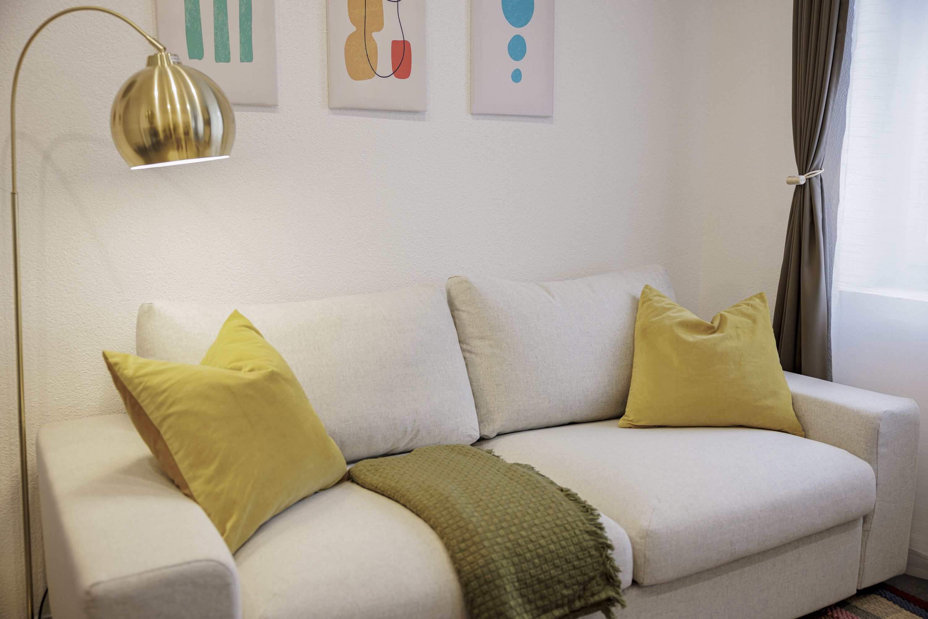 Un sofá blanco con dos almohadas amarillas y una manta verde.