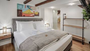 A modern bedroom with a large bed, a wooden headboard, a painting on the wall, and a loft-style staircase.