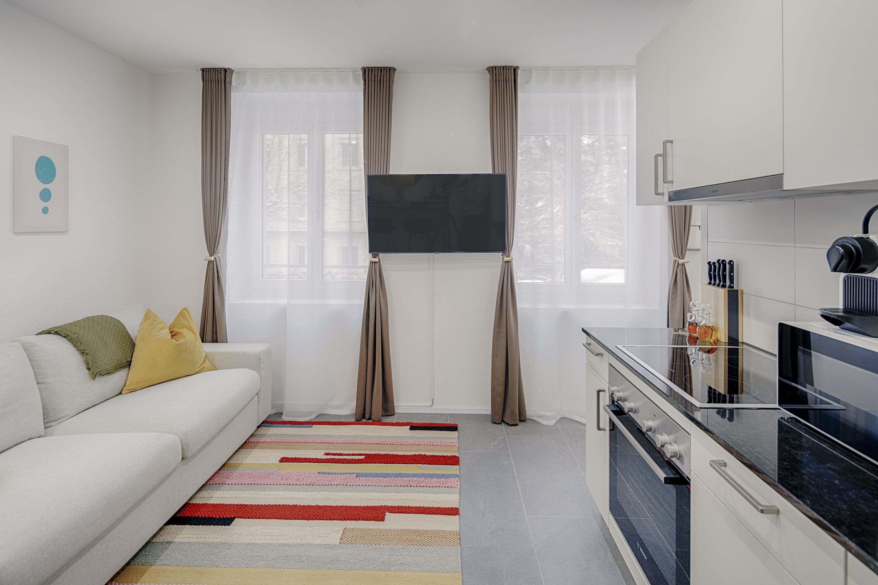 Une cuisine moderne dotée d’un téléviseur à écran plat, de meubles blancs et d’un tapis à rayures.
