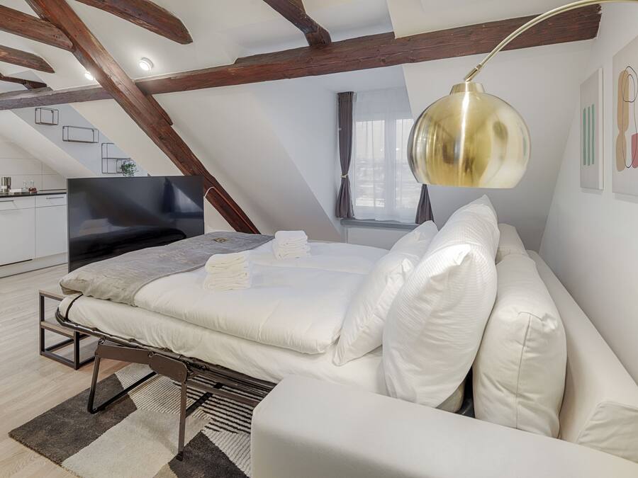 Een moderne loft slaapkamer met een groot bed, een televisie en een eethoek, zichtbaar door een open deur.