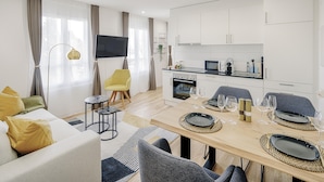 Una sala de estar moderna con un sofá, una mesa de comedor preparada para cuatro personas y una cocina con armarios y electrodomésticos blancos.