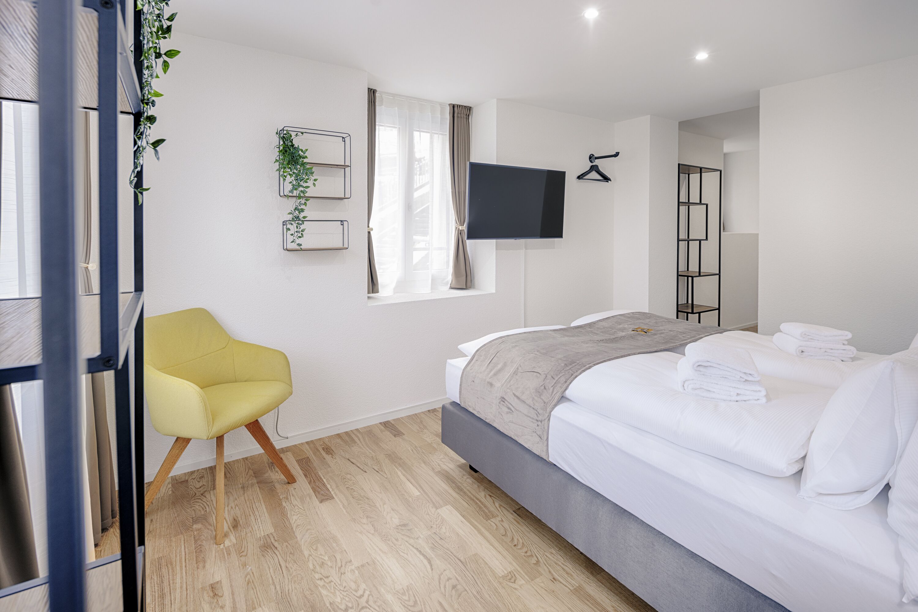 Una habitación de hotel moderna con cama, una silla, un televisor y un ventanal con cortinas.