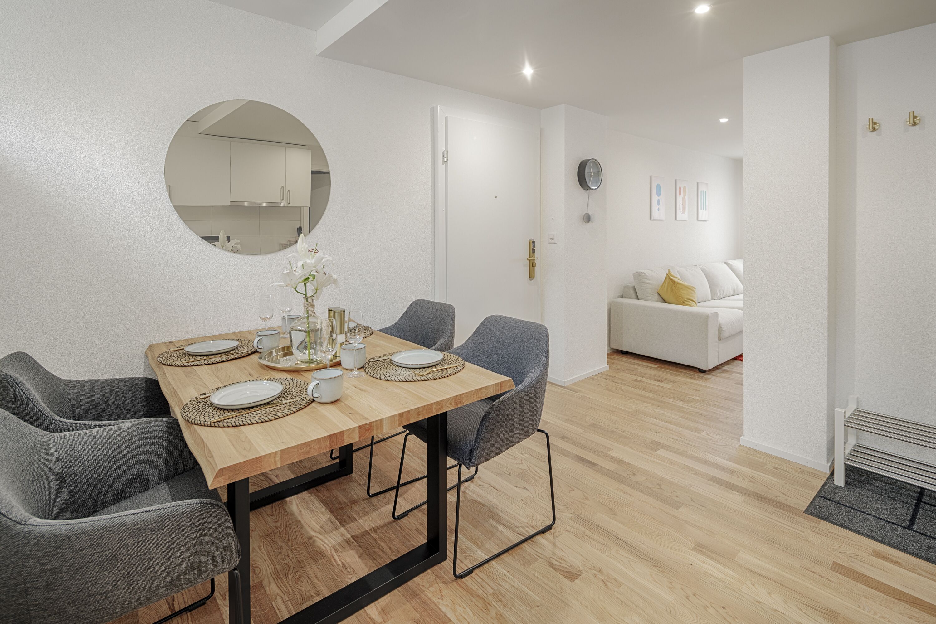 A modern dining area with a wooden table, grey chairs, and a round mirror on the wall.