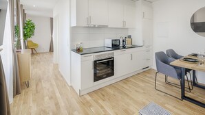 Una cocina moderna con muebles blancos, horno empotrado y zona de comedor con mesa y sillas de madera.