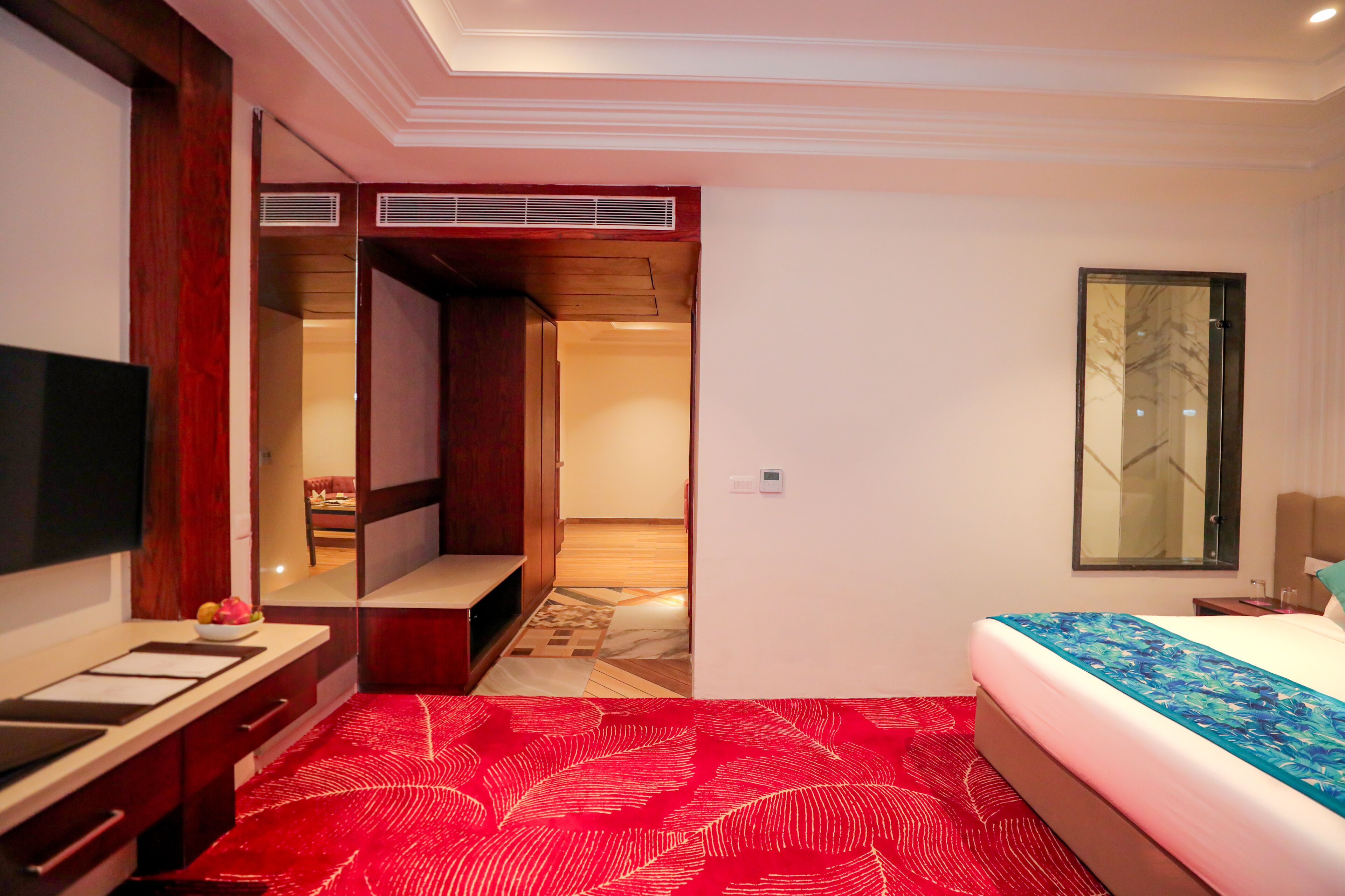 A hotel room with a bed, a TV, a desk with a mirror, and a wardrobe.