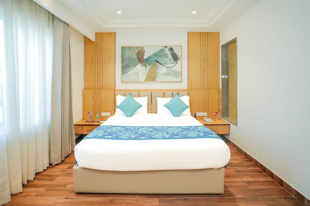 Habitación de hotel con una cama grande, paneles de madera en las paredes, un cuadro sobre la cama y una mesita de noche con un teléfono y flores.