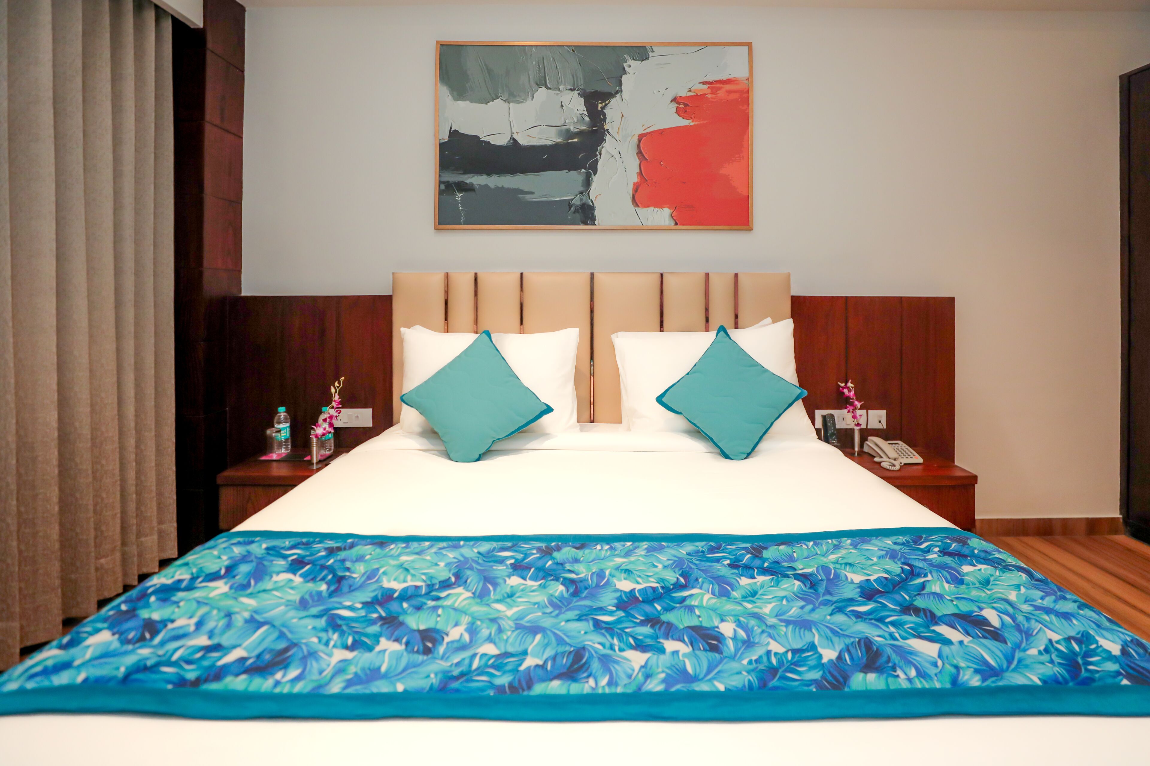 A hotel room with a large bed, two pillows, a nightstand, a telephone, and a painting on the wall.