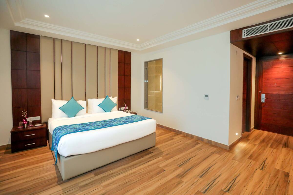 Una habitación de hotel moderna con una cama grande, suelo de madera, un armario empotrado y un espejo amplio.