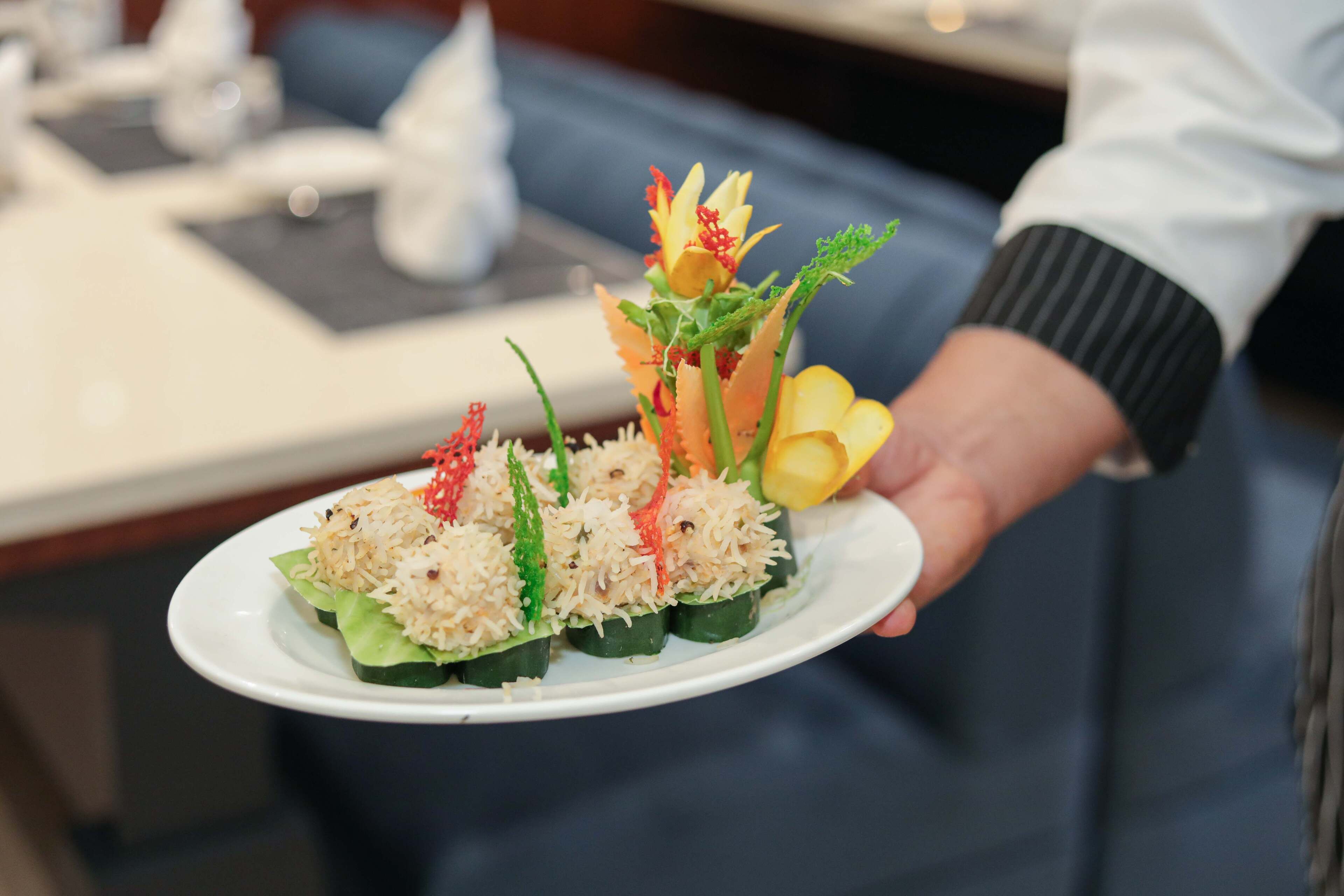 Un plato con una disposición de alimentos, que incluye arroz, verduras y guarniciones, sostenido por una persona.