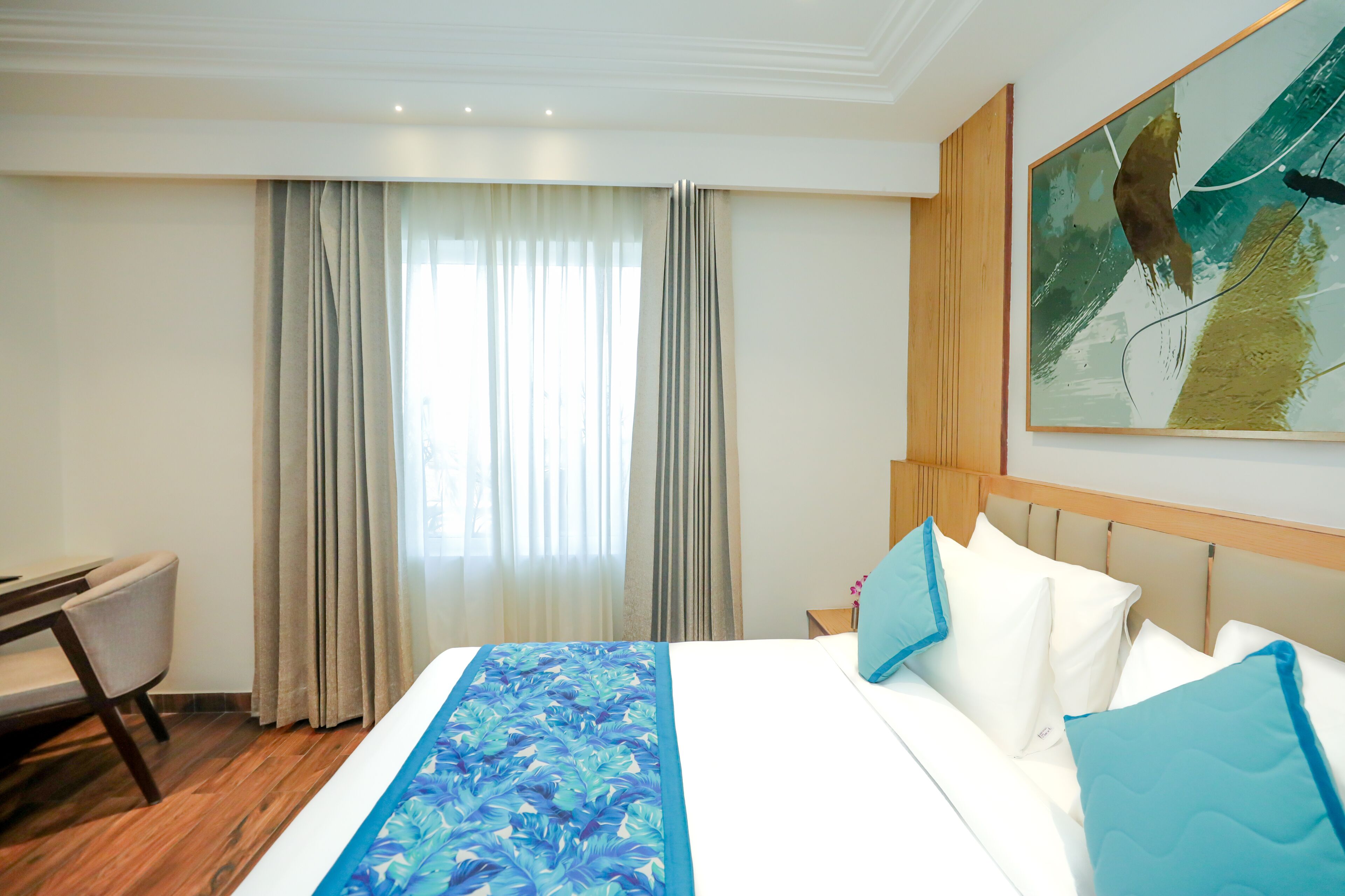 A hotel room with a bed, a desk, and a large window with curtains.