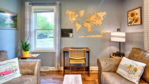 A cozy living room with a world map on the wall, a wooden table, two leather sofas, and a small desk with a chair. - Laurna Dune (Gary)