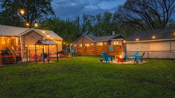A fenced backyard with a lawn, a wooden cabin, and a metal shed. - Laurna Dune (Gary)