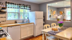 A kitchen with a wooden countertop, white cabinets, a refrigerator, and a dining area with a table and chairs. - Laurna Dune (Gary)