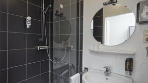 Ein modernes Badezimmer mit einer gläsernen Duschkabine, einem runden Spiegel, einem weißen Waschbecken und einem Handdesinfektionsmittelspender.