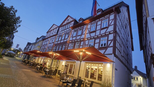 Ein traditionelles europäisches Gebäude mit Innenhofcafé, Außenbestuhlung und Sonnenschirmen.