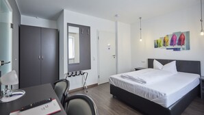 Ein modernes Hotelzimmer mit einem großen Bett, einem Schreibtisch mit Stuhl, einem Spiegel und einem Bild von High Heels an der Wand.