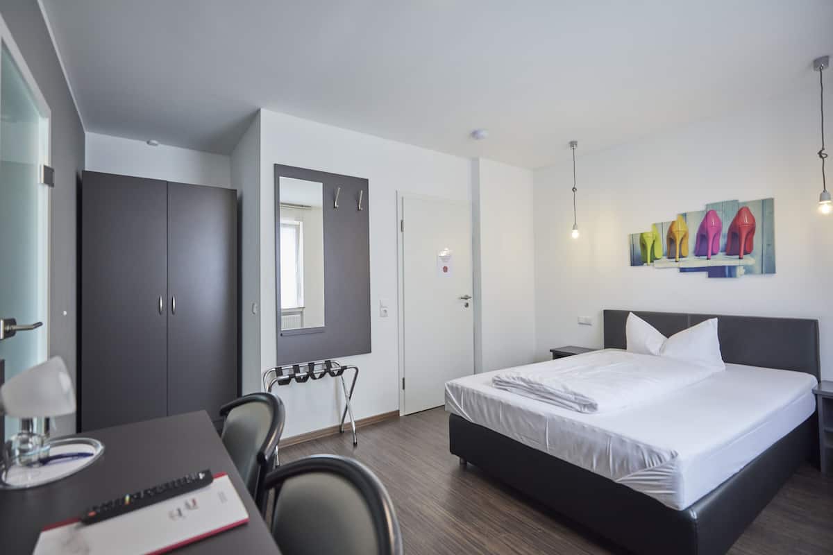 Ein modernes Hotelzimmer mit einem großen Bett, einem Schreibtisch mit Stuhl, einem Spiegel und einem Bild von High Heels an der Wand.