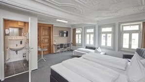 Ein Hotelzimmer mit einem großen Bett, einem Schreibtisch, einem Fernseher und einem Badezimmer mit Waschbecken und Spiegel.