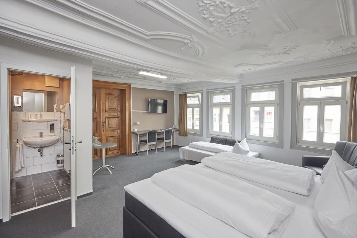 Ein Hotelzimmer mit einem großen Bett, einem Schreibtisch, einem Fernseher und einem Badezimmer mit Waschbecken und Spiegel.
