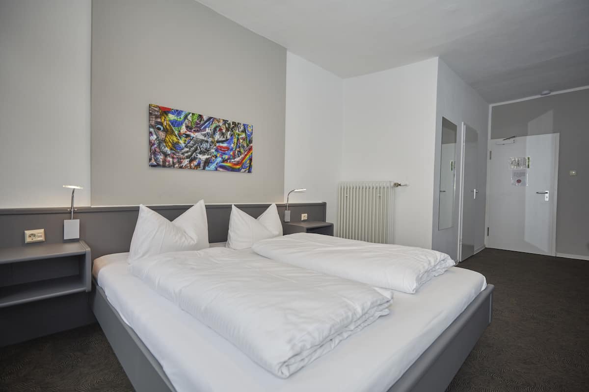 Ein modernes Hotelzimmer mit einem großen Bett, einem Nachttisch, einem Heizkörper und einer Tür zu einem anderen Raum.