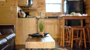 Interior acolhedor de uma cabana com uma mesa de jantar de madeira, uma pequena planta em vaso e um sofá de couro.